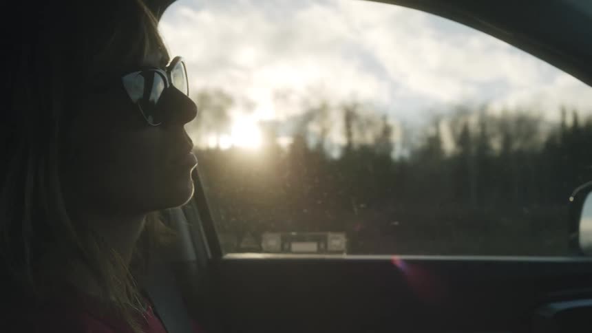 A woman driving a car at sunrise with rays of sunlight shining through the window