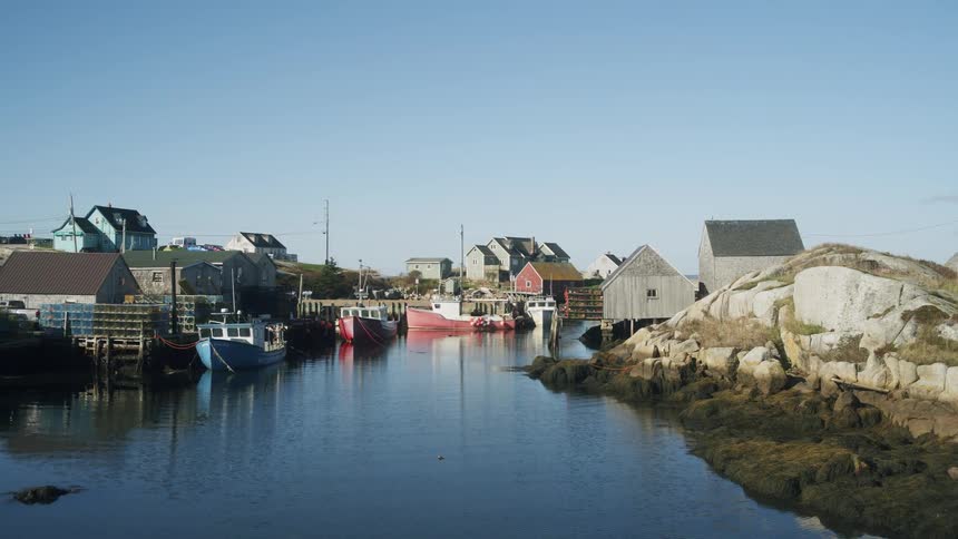 A canal running through a small town at midday with boats neatly docked along the edge as sunlight reflects off the calm water and the surrounding buildings cast soft short shadows across the scene