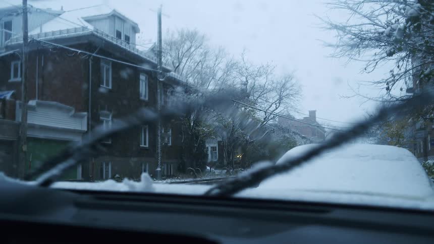Video two windshield wipers sweep across the frame they move upward from the bottom of the screen around the 5second mark clearing a path through the light snow and moisture on the glass before disappearing back downthe lines of the wipers are dark