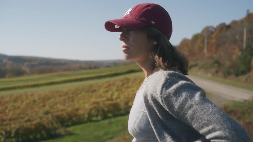 A woman on face cap stands on a hill at midday typing on a smartphone