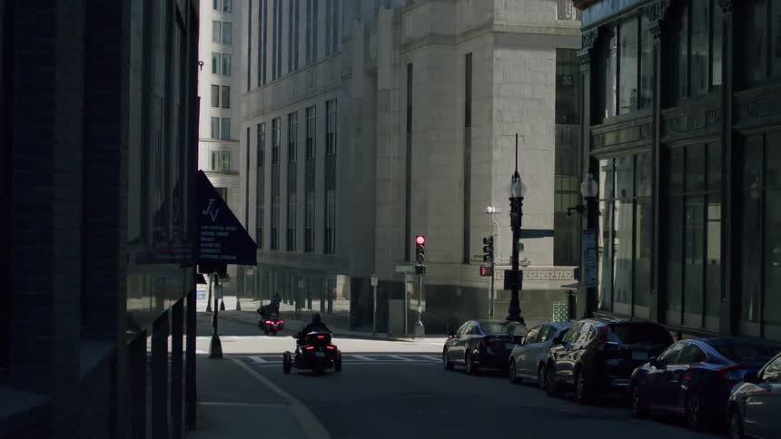 An empty city street with moving motorcycles and parked cars at midday