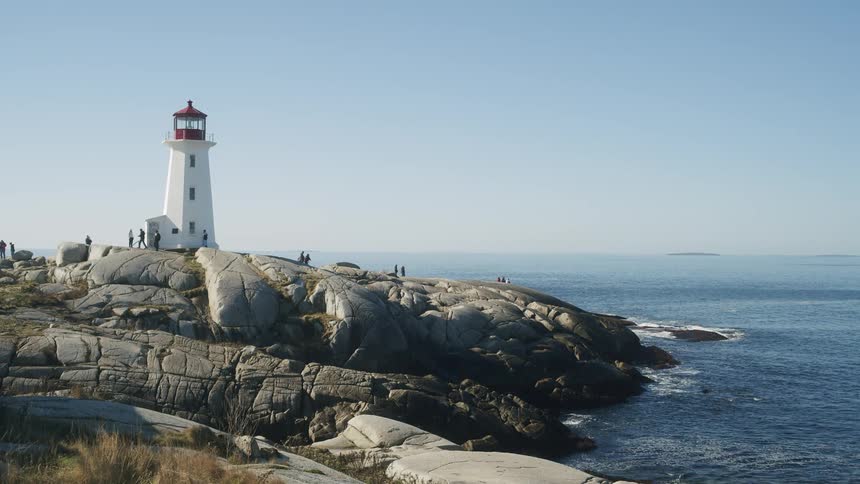 Lighthouse overlooking the water as people walk on the rocky coast