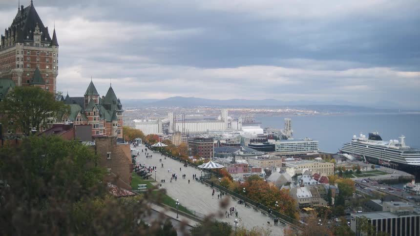 Historic city seen from an elevated viewpoint with old buildings an active harbor and docked ships under a cloudy sky