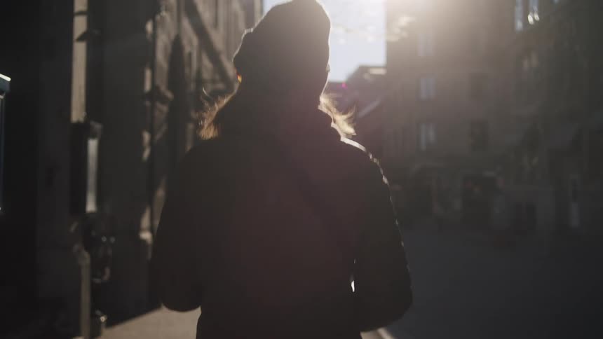 Woman wearing a jacket and a hat is walking through the city