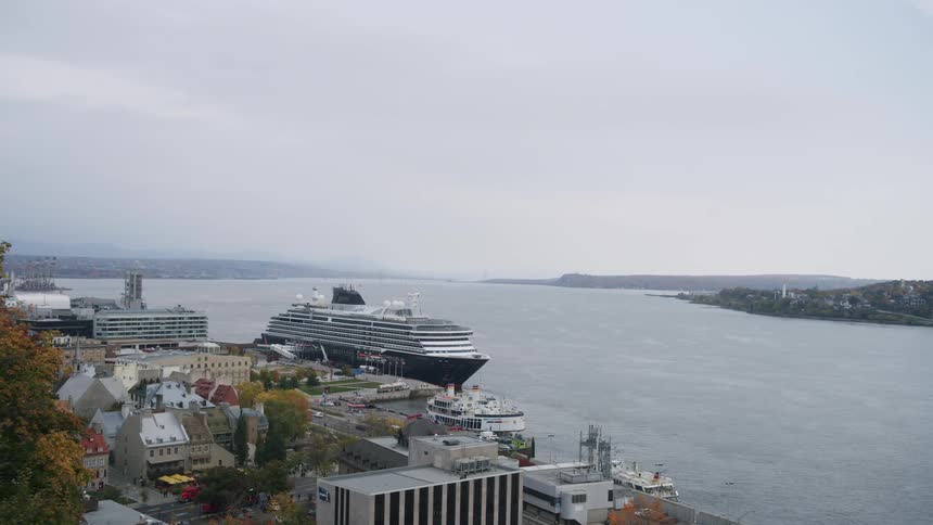 The video shows a wide static shot of a large black and white cruise ship docked at a port in a coastal city