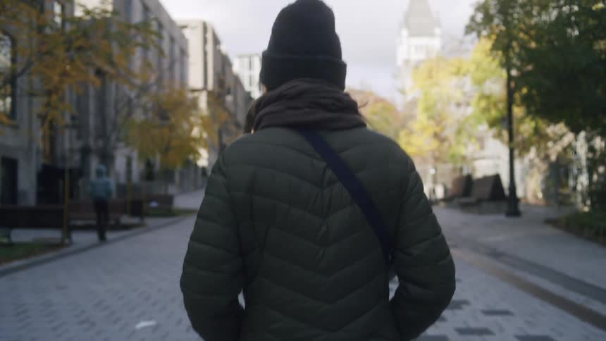 Woman in a jacket walking through a square in an urban city