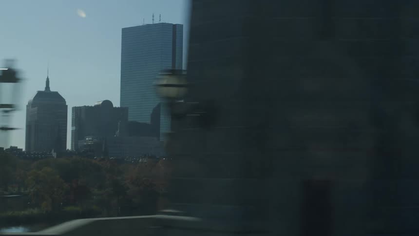 The boston skyline and charles river pass by as seen from a moving vehicle crossing a bridge