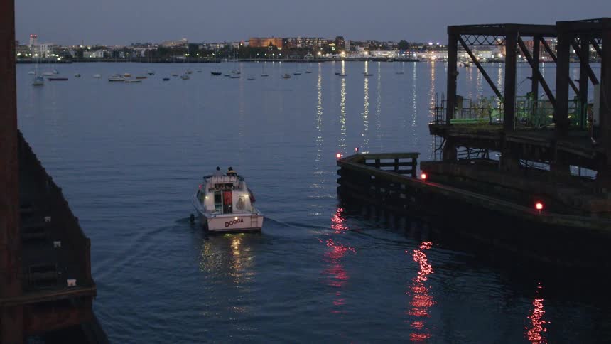 Boat on a lake next to a dock with other boats and a metropolitan area on the background outdoors during dusk or dawn