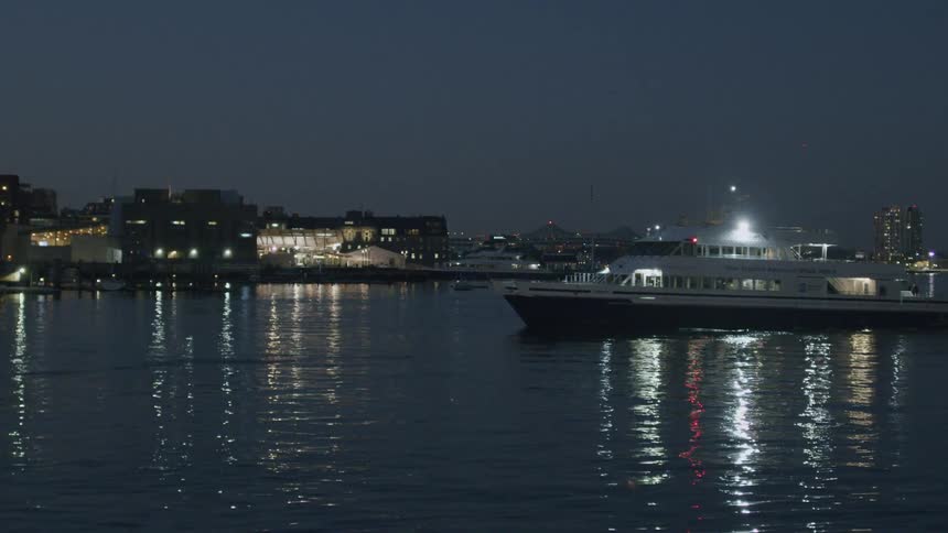 The wake of the ferry as it moves across the water cutting through the reflections of the city lights