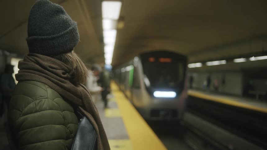 Woman in a jacket and hat waiting for a train at a subway station