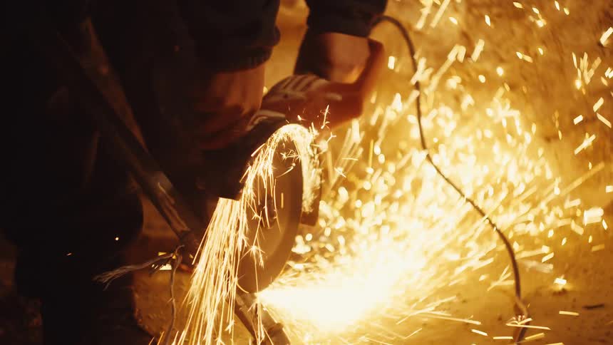 Person operating grinder on metal piece with intense sparks