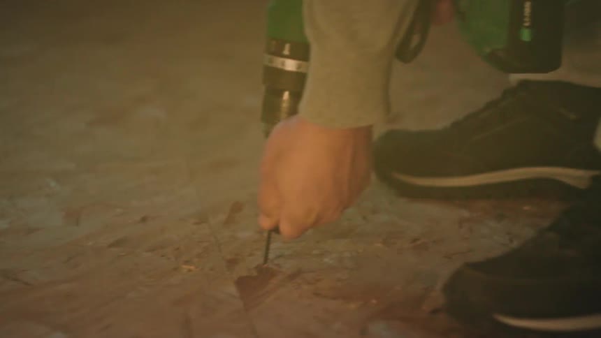 Person using power drill to screw into wooden surface indoors