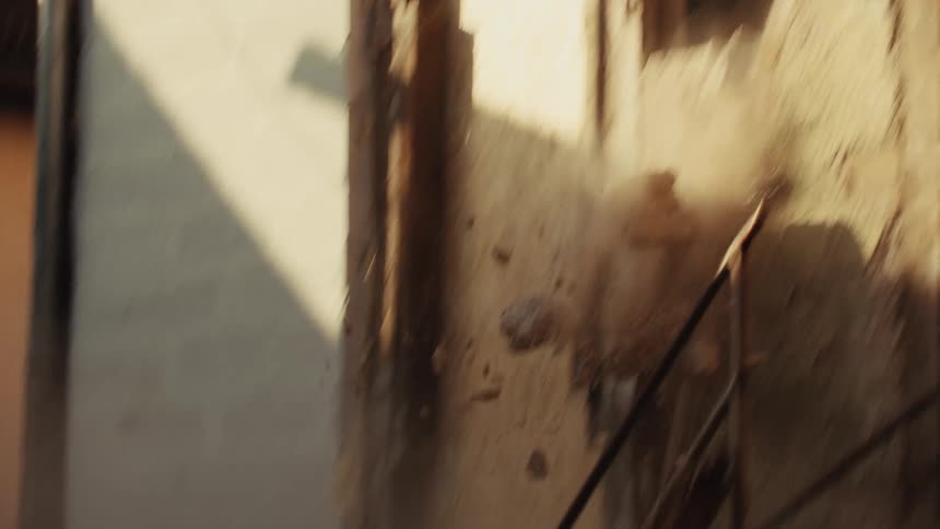 A dilapidated building wall made of mud and timber frames begins to crumble and collapse inwardthe structure falls apart rapidly sending a thick cloud of dust and debris into the air as the camera pans downward