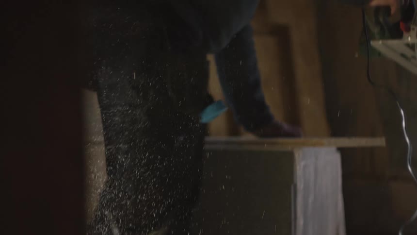 A carpenter uses a circular saw to cut through a piece of wood sending a spray of sawdust into the airthe worker then steps away from the workbench as the dust continues to fall in the dimly lit workspace