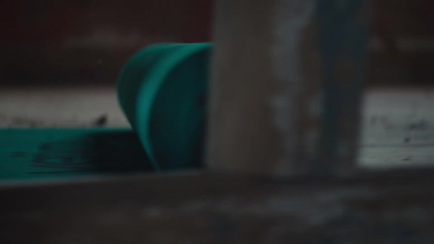 A persons hands are shown unrolling a roll of bright teal mesh material across a dark dusty wooden floorthe camera focuses closely on the textured roll as it moves highlighting the contrast between the vibrant material and the debriscovered surfac