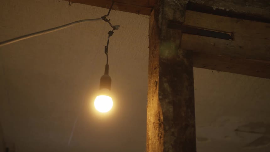 A warm bulb hanging from the ceiling inside a room glowing softly while its connecting wires dangle loosely to the side