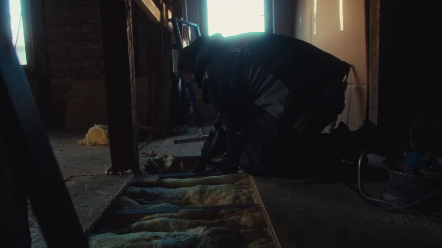 Person kneeling installing insulation between floor joists in construction