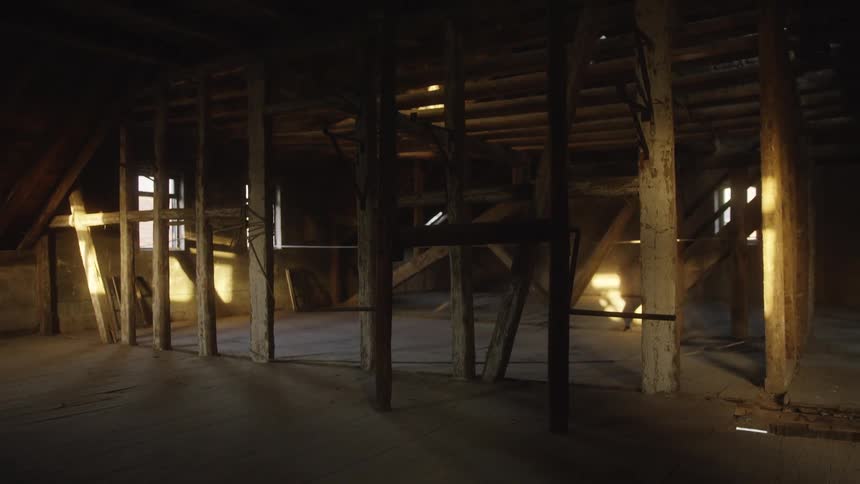 Warm lateafternoon sunlight streams through small windows casting long geometric shadows across the dusty floor of an old wooden atticthe stationary camera captures a silent empty space filled with weathered support beams and a rustic timber roof