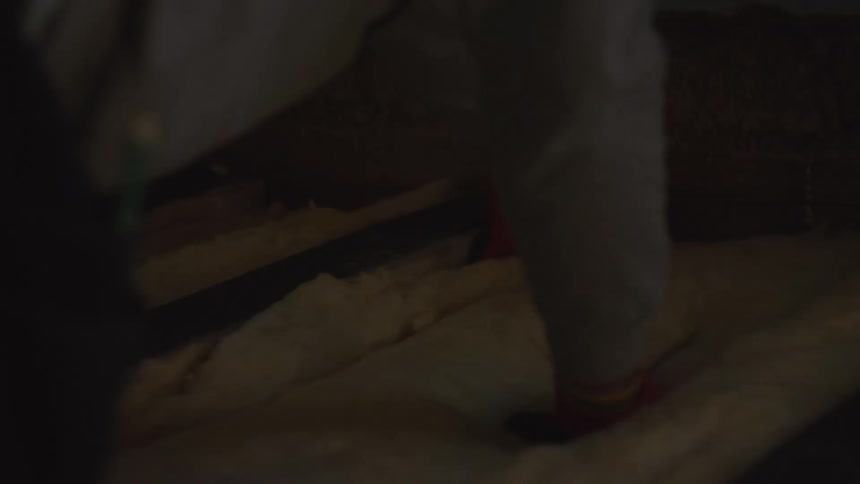 A worker in a protective suit installs fiberglass insulation in a dimly lit attic