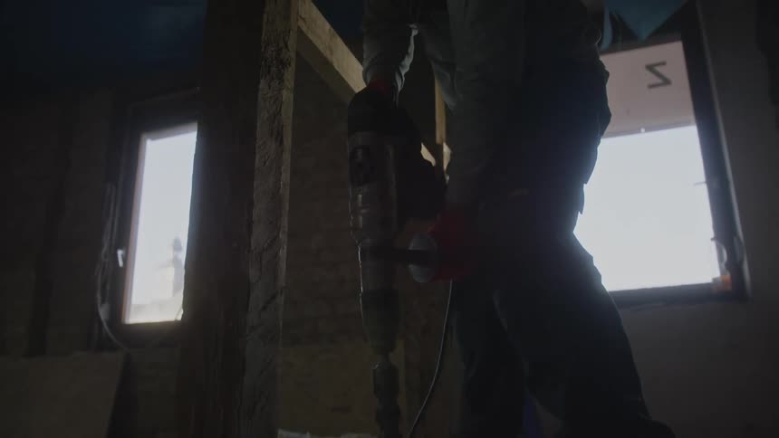 The construction worker is drilling into the floor