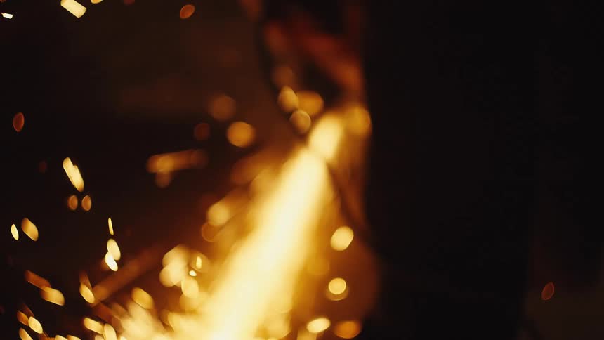 In this video a person is using an angle grinder to cut through metal creating a bright stream of orange sparks the camera focus shifts from a blurry closeup to a clear view of the tool and the gloved hands of the worker