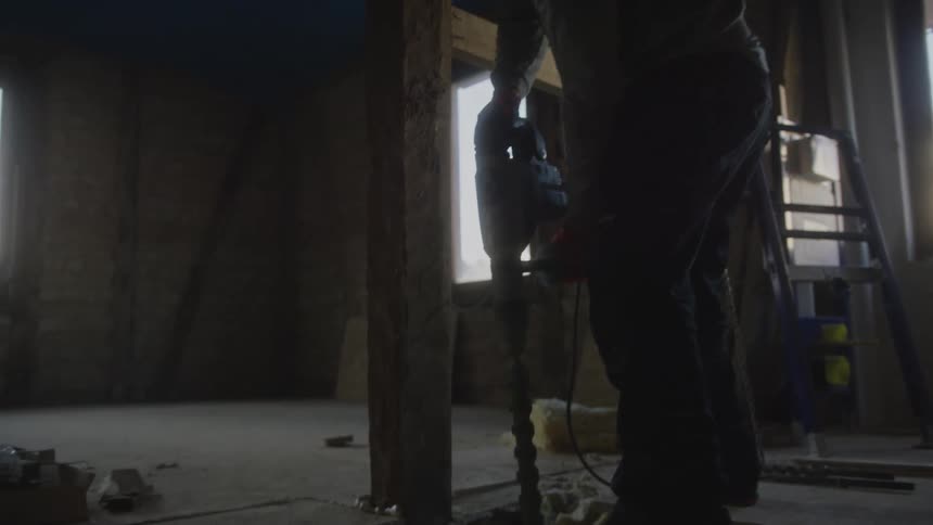 Person using drill on wooden beam in room under renovation