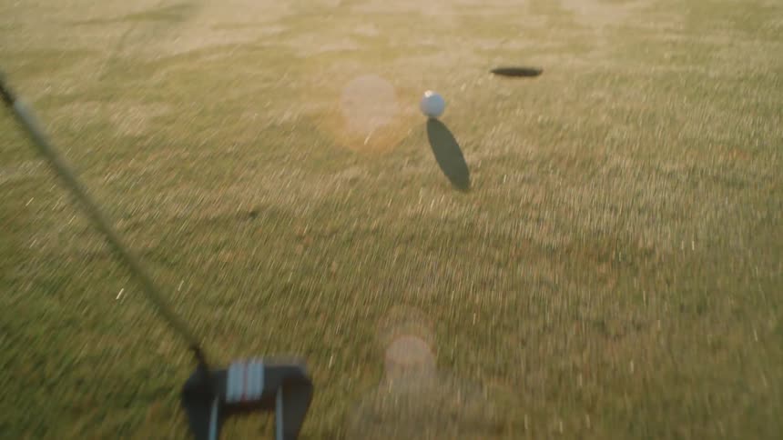 Man holds a golf club and hits the ball missing the hole