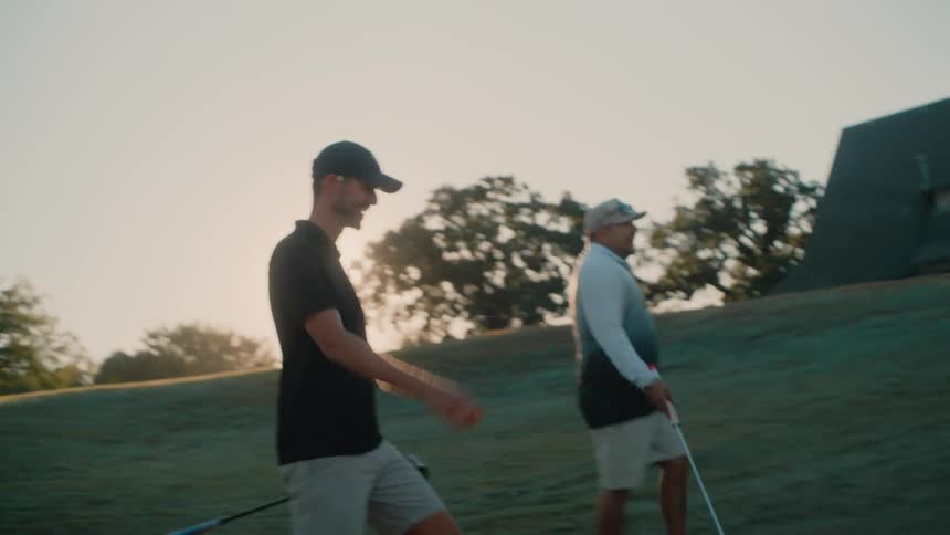 Two men walk across the field with their golf clubs