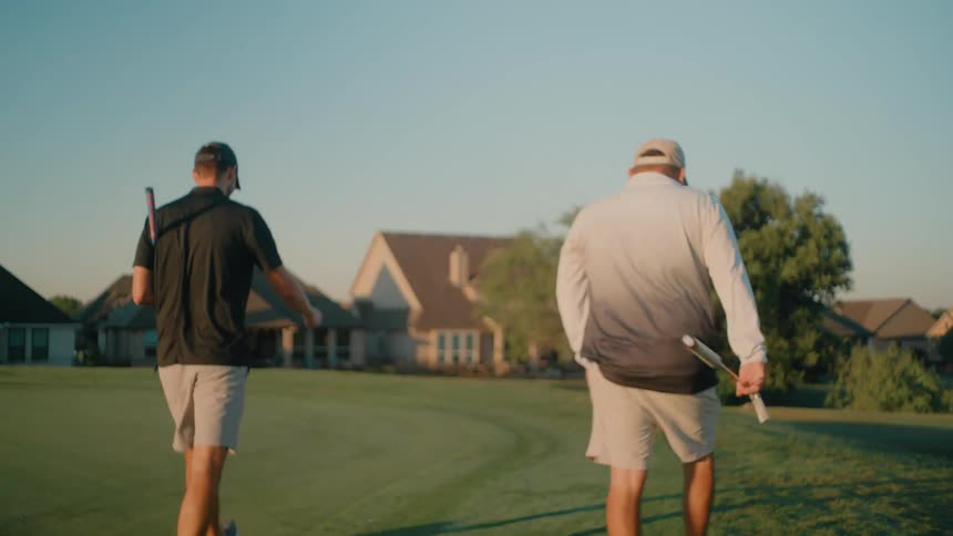 Two men with a golf club walking across a golf course