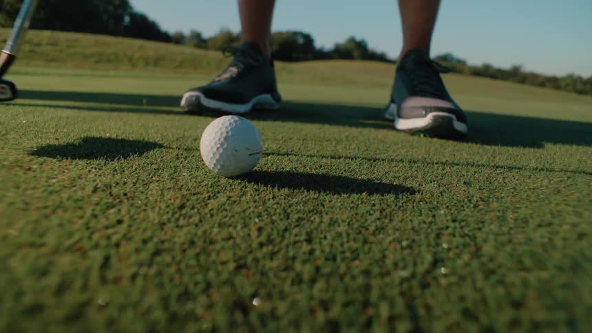 Feet of a male golf player hitting a ball on a golf course outdoors during day time