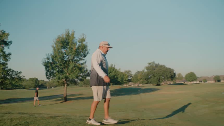 Adult male golf player wearing a cap walking on the field near another male player outdoors