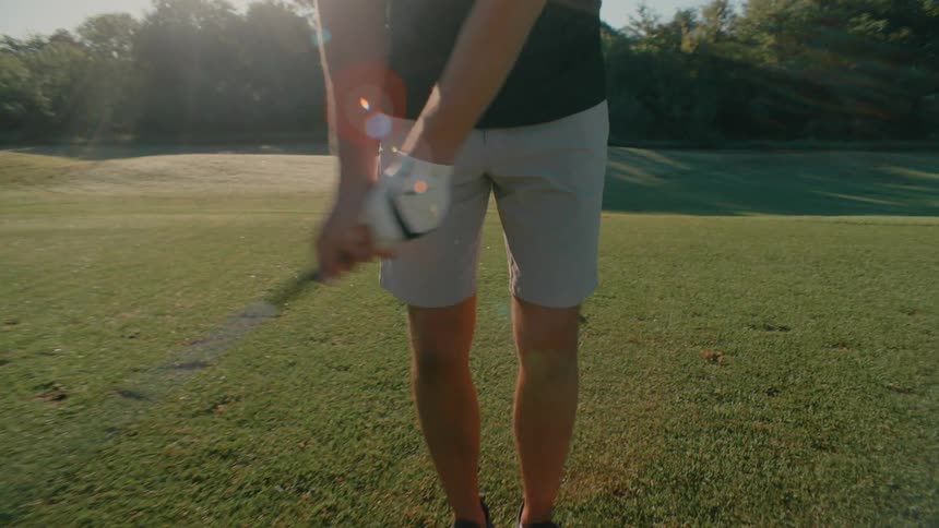 A golfer stands on a sundrenched green carefully adjusting his grip on the club as he prepares for a shot the low afternoon sun creates a warm glow and casting long shadows across the grass while the camera moves in for a closeup of his hands