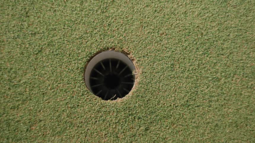 A golf ball rolling past a cup