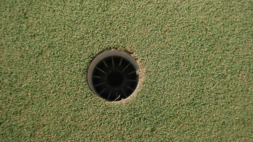 A topdown view shows a clean dark golf hole set into a textured green putting surface the surrounding grass appears short and uniform typical of a wellmaintained golf course green