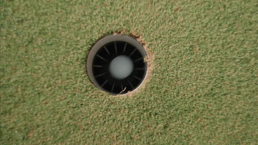 Golf ball rolling into a hole outdoors during day time