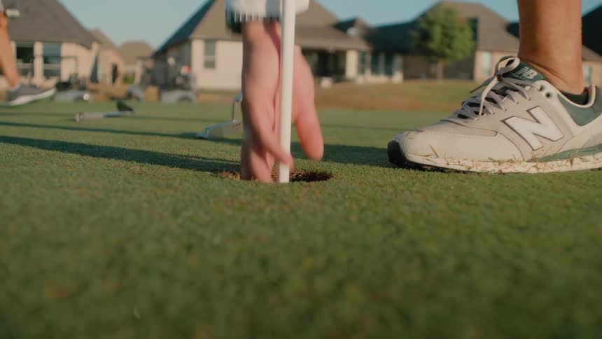 Person takes a swing and hits the target in golf then catches the ball with their hand