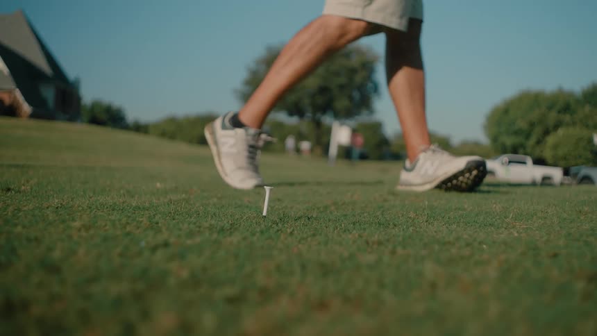 A golf player swings at the ball with the club at midday sending it flying out across the course