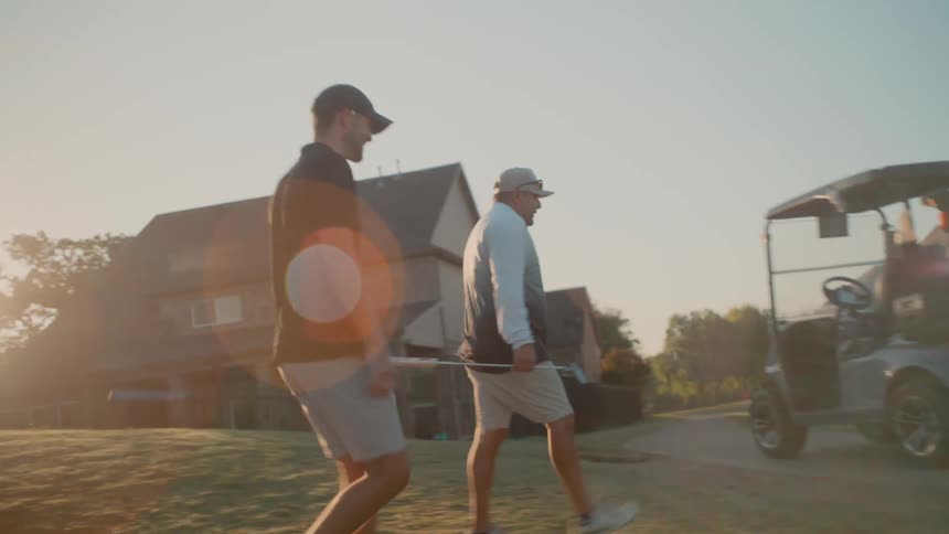 A long thin straight line held by the man in the black shirt as he walks toward the golf carta slanted diagonal line in the background that forms the silhouette of the residential building against the sky