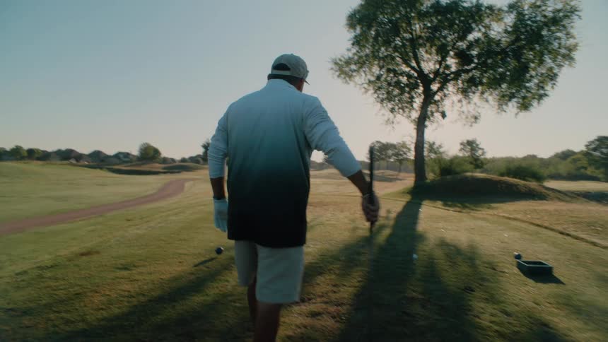 Man stands on the field with his golf club and walks over to the golf ball