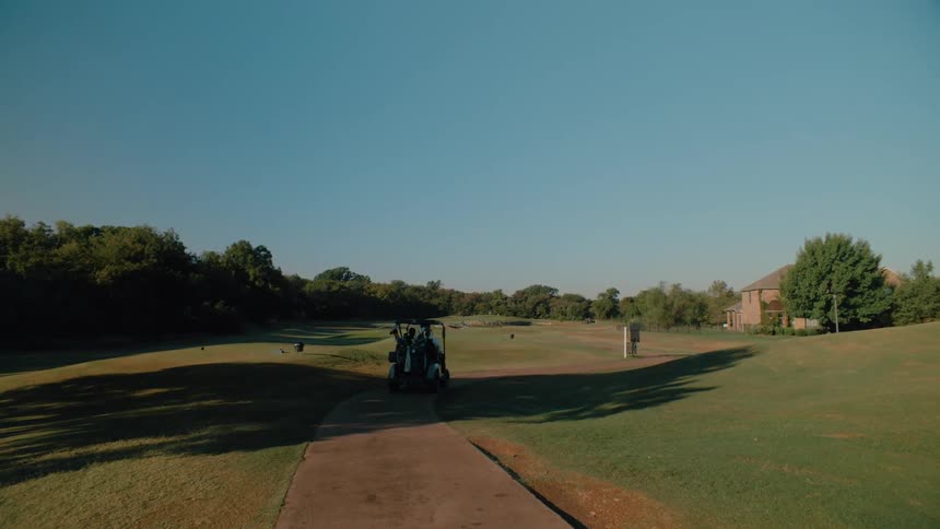 A golf cart moving across the golf course on a sunny day rolling over trimmed grass with clear skies overhead