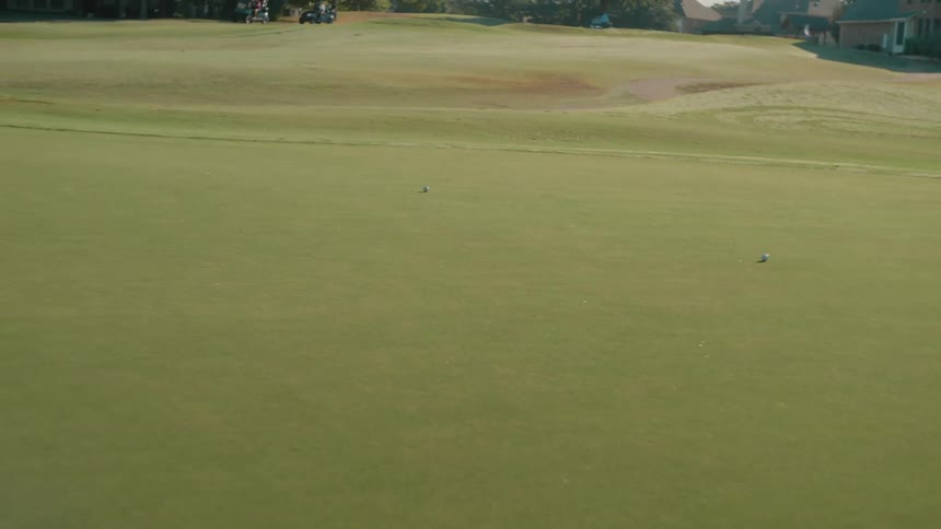 A golf ball rolling across the course toward the hole at midday