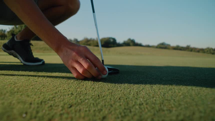 Male golf player positioning a ball on the field next to another golf player outdoors during day time