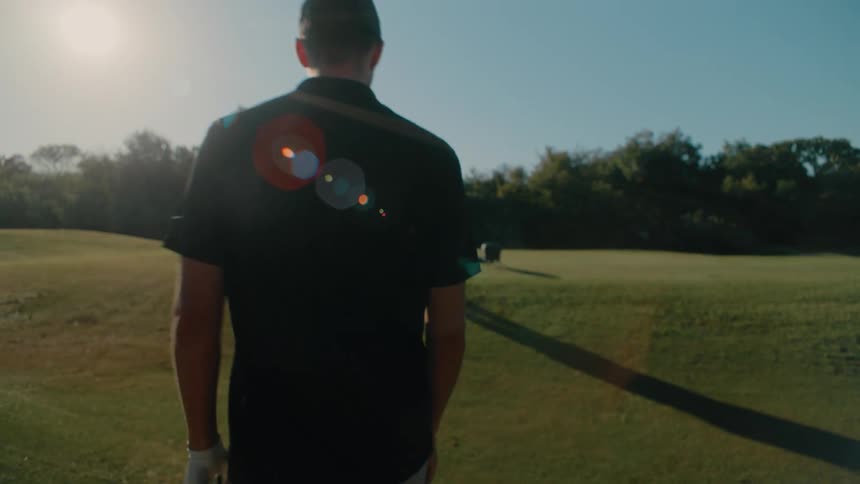 Man takes a golf club out of the back in back of the golf cart and walks across the field