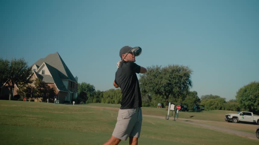 A young golf player on a course at midday wearing a hat and swinging his club to hit the ball