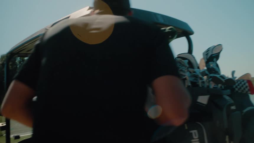 A couple men grab golf clubs out of the back of a golf cart