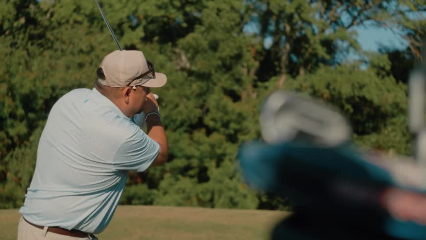 Man stands holding his golf club as he swings and watches the ball fly