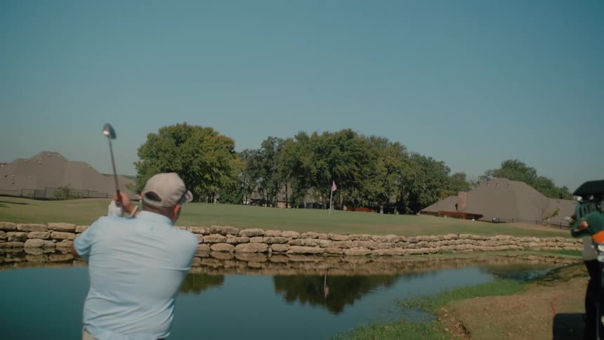 Man in a cap takes a golf swing across a lake