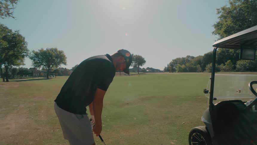 Golfer prepares a shot on a grassy area next to a golf cart