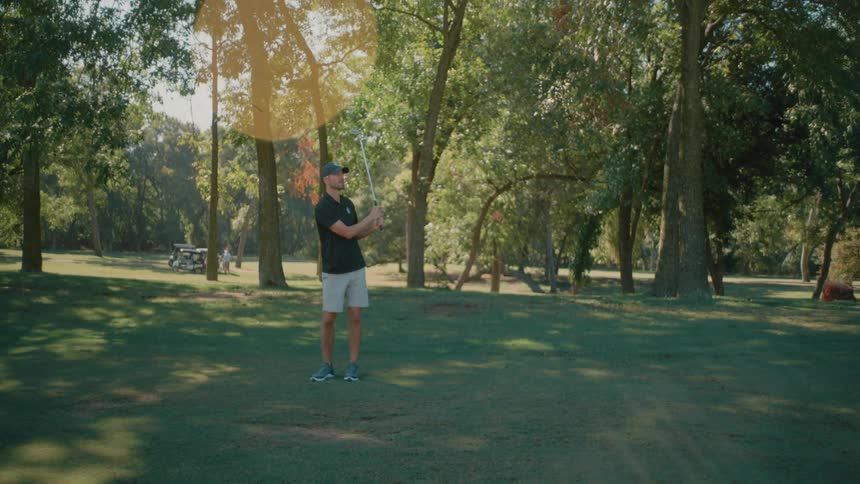 Man stands on the golf course and swings his golf club hitting the golf ball