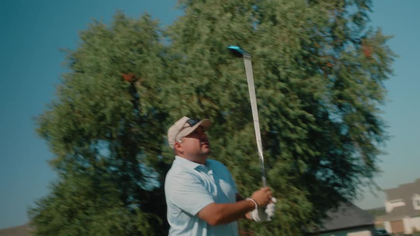 Man stands holding his golf club as he swings and hits the ball